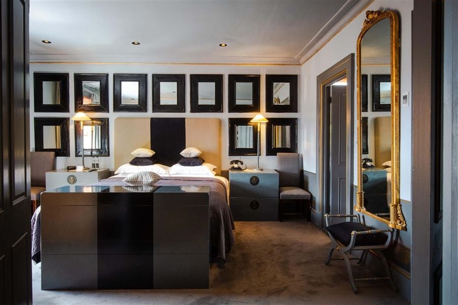 Elegant townhouse suite with plush velvet headboard, ornate gold-framed mirror, and sophisticated dark blue walls at luxury boutique hotel