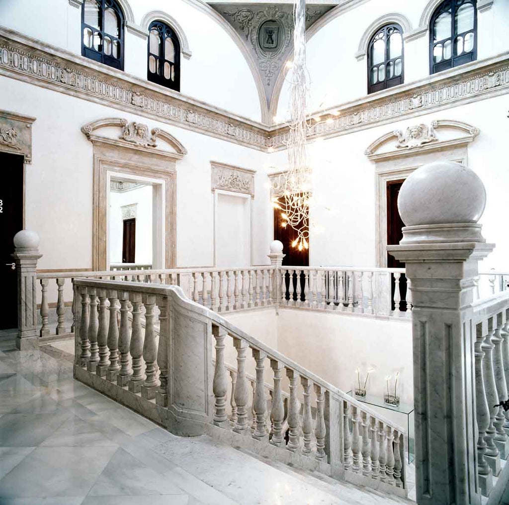 Elegant 19th-century palace hotel with white stone facade, ornate balconies, and manicured garden surrounded by palm trees in Granada