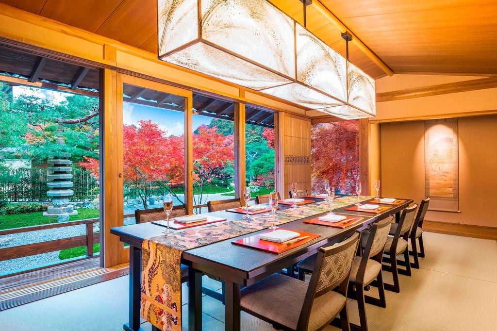 Traditional Japanese ryokan with elegant wooden exterior, stone garden, and bamboo fencing set against lush mountainside in Arashiyama, Kyoto