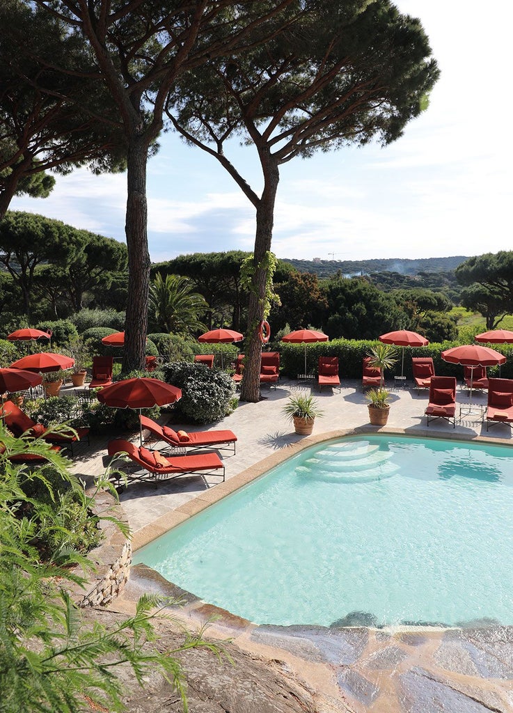 Luxurious Mediterranean villa with white facade, lush tropical gardens, and elegant blue and white striped sun loungers overlooking Saint-Tropez coastline