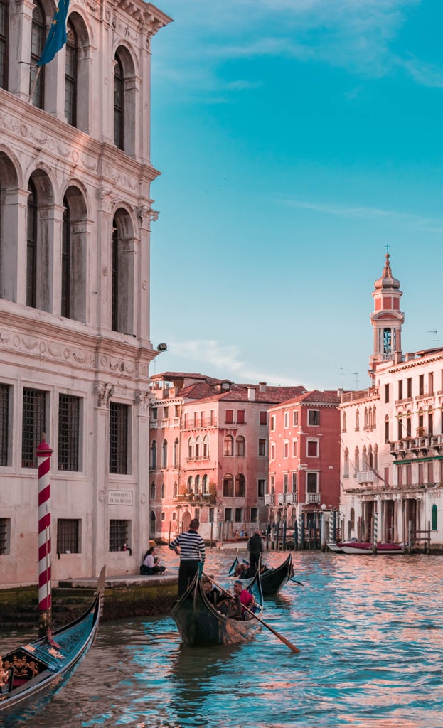 Traditional wooden gondola gliding through narrow Venice canal at sunset, ornate golden decorations gleaming against historic palazzo walls