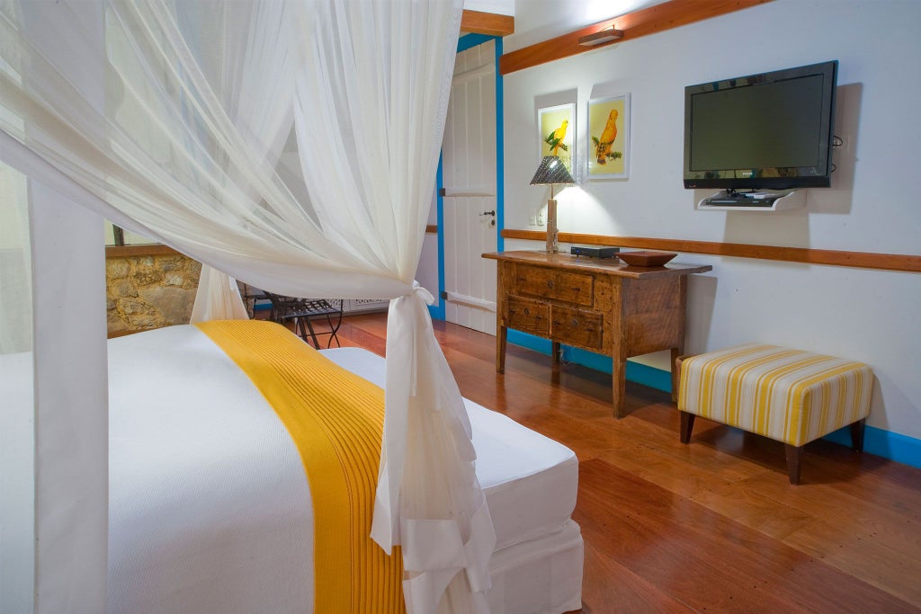 Luxurious yellow-themed hotel suite with elegant colonial-style decor, white linens, and vibrant turquoise accents in a Brazilian boutique hotel room