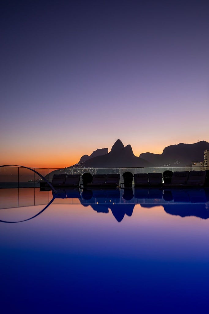 Luxurious rooftop pool overlooking Ipanema Beach, with sleek design and panoramic Rio de Janeiro skyline at sunset, embodying elegant Brazilian hospitality