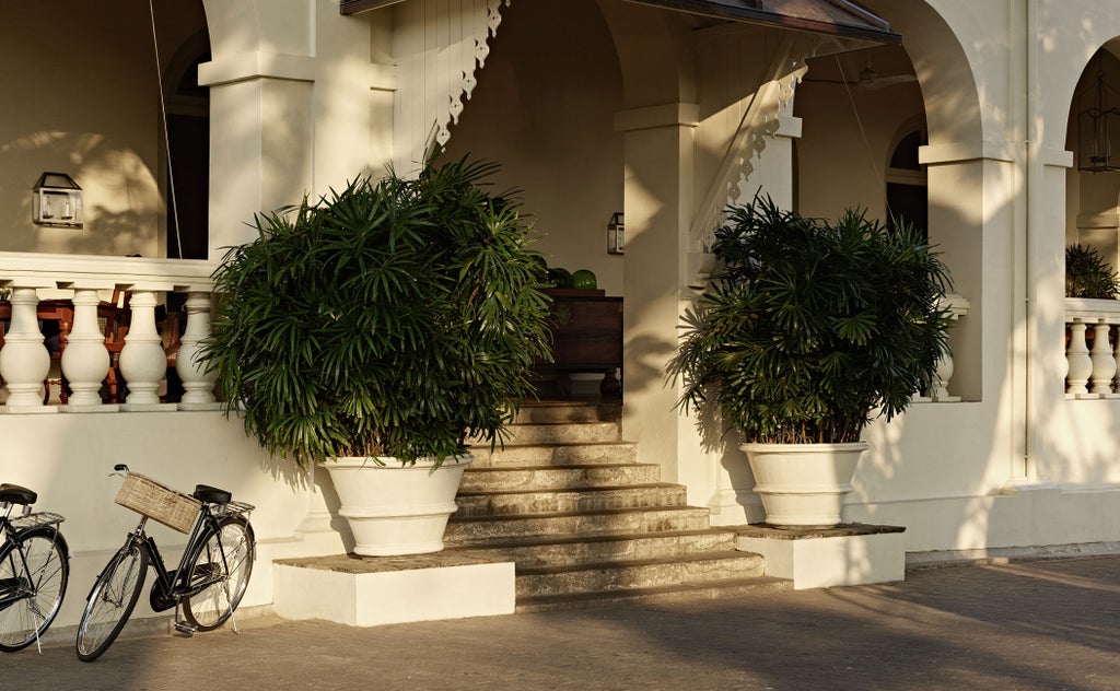 Elegant colonial-era hotel facade at sunrise, with palm trees and white columns framing ornate balconies and antique shuttered windows