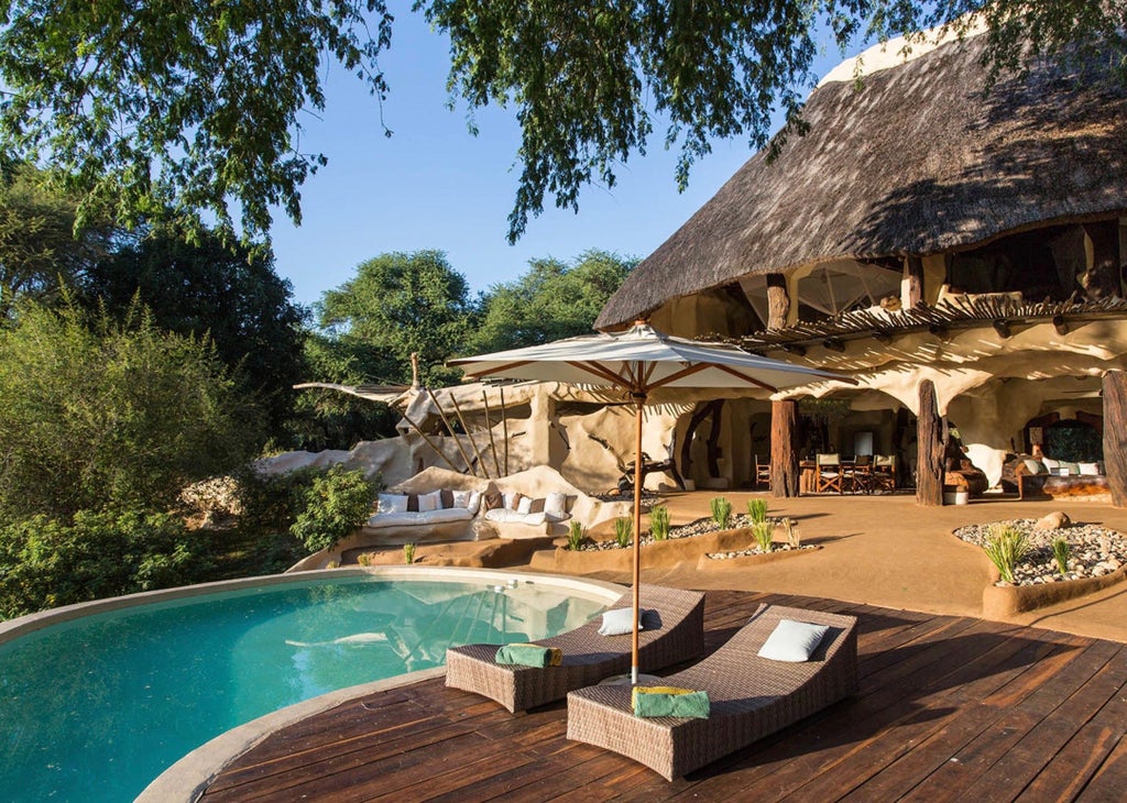 Luxurious open-air riverside villa with thatched roof and natural stone walls nestled among trees overlooking Zambezi River at sunset