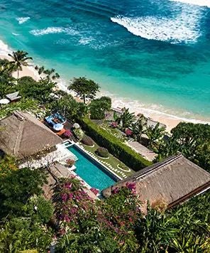 Luxury beachfront resort with traditional thatched-roof villas nestled on a lush cliff overlooking pristine turquoise waters of Sumba Island, Indonesia