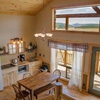 Rustic wooden lodge room with plush bedding, mountain views through large windows, southwestern decor, and warm earthy color palette at Scenset Mountain Ranch