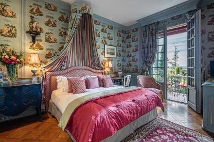 Luxurious French hotel room with soft white linens, antique furnishings, ornate chandelier, and delicate blue-gray color palette in Provence-style elegant accommodation