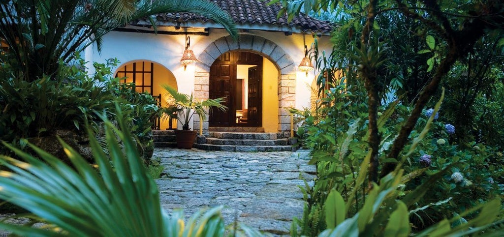 Luxurious stone-built villa nestled in Andean cloud forest, featuring rustic wood accents, lush gardens and mountain backdrop