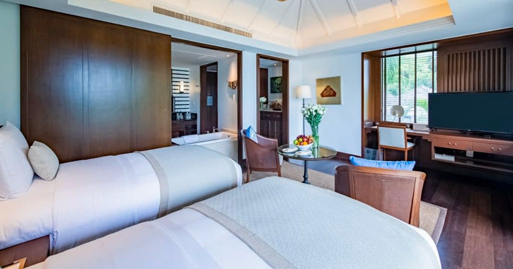 Spacious Thai-style pool suite bedroom with king bed, teak furnishings, white linens, and floor-to-ceiling windows overlooking private pool