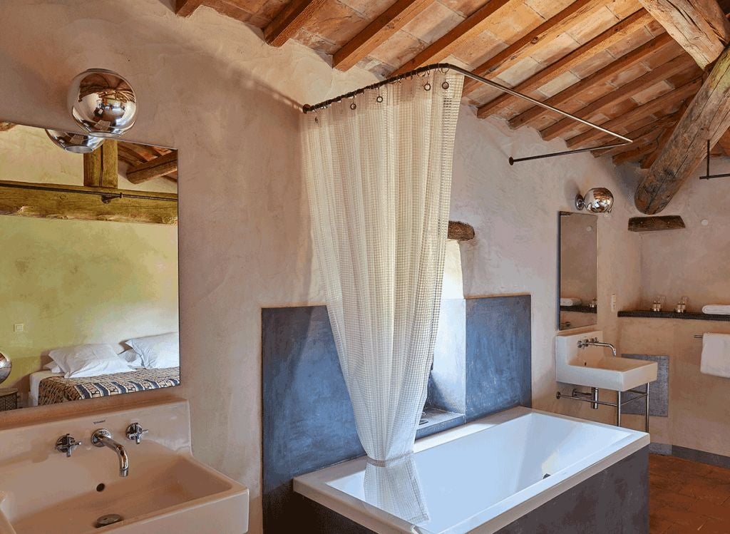 Elegant stone-walled bedroom in French countryside hotel, with plush white linens, antique wooden furniture, and soft natural light streaming through arched window