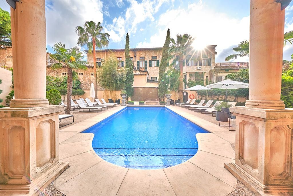 Luxurious Mediterranean hotel with stone facade, white balconies, and lush greenery nestled in scenic Sóller valley, Mallorca, Spain