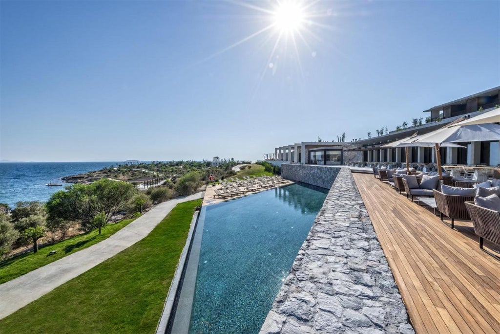 Modern luxury resort with infinity pool overlooking the Aegean Sea, set against rugged cliffs and Mediterranean landscape at sunset