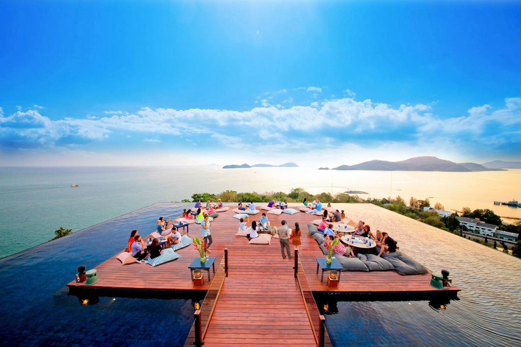 Luxurious infinity pool overlooking Andaman Sea at sunset, with modern glass-walled villas nestled among tropical palm trees