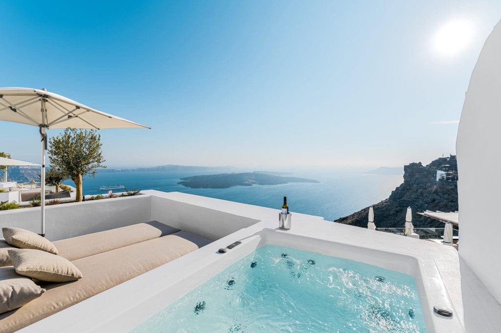 Luxurious white cave-style hotel nestled on Santorini's cliffside, featuring elegant blue-domed architecture and stunning Aegean Sea panorama at sunset