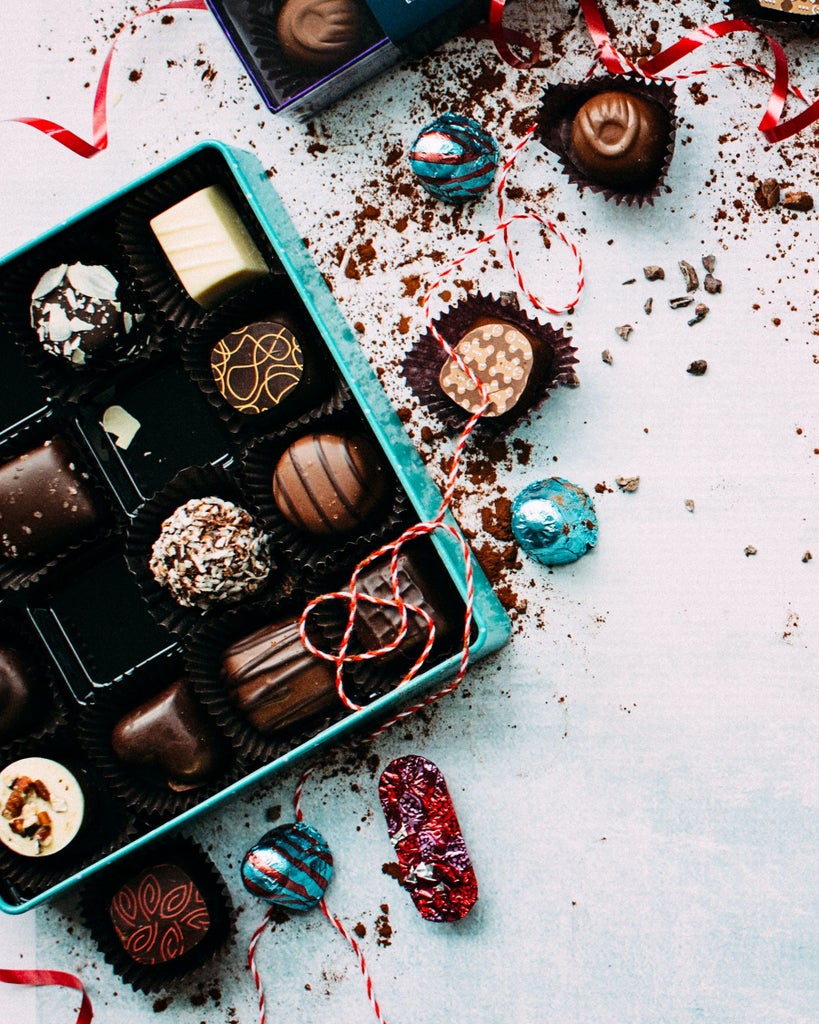 Four decadent Swiss pralines on marble counter at artisan chocolate shop, showcasing gold leaf and intricate hand-painted designs