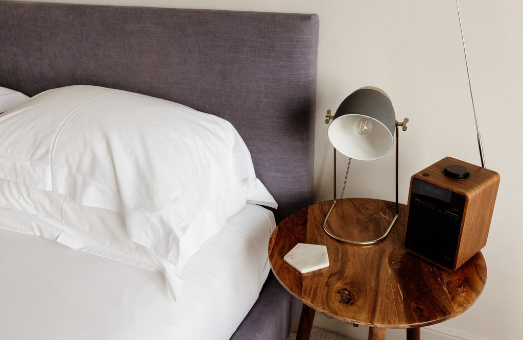 Elegant coastal-themed hotel bedroom with crisp white linens, soft blue accent pillows, and panoramic seaside view through large windows at The Sandy Duck