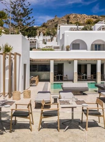 Luxurious whitewashed hotel overlooking azure Aegean waters, with minimalist design, private balconies, and stunning Mykonos landscape in background