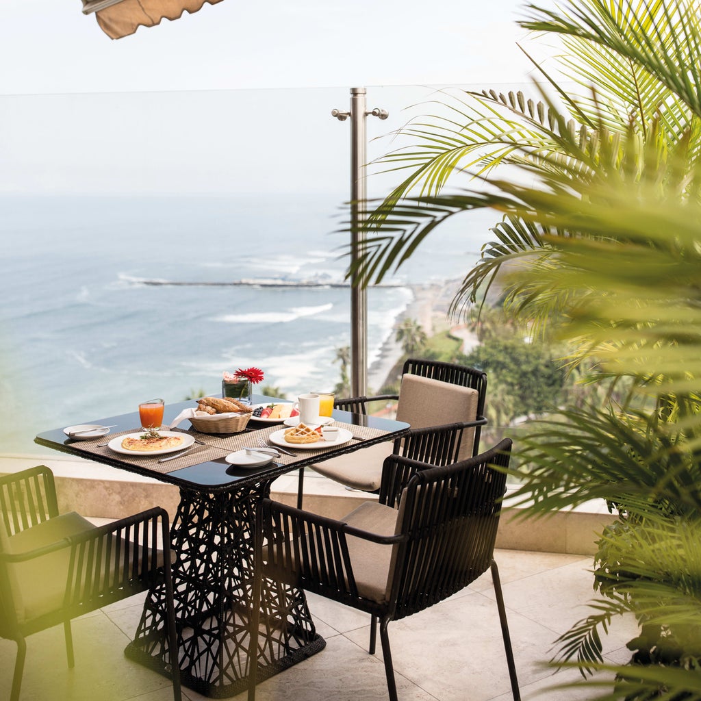 Elegant high-rise hotel overlooking Pacific Ocean in Lima's upscale Miraflores district, featuring palm-lined terraces and infinity pool