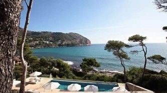 Elegant cliff-side luxury hotel overlooking turquoise Mediterranean waters, with stone architecture and pristine infinity pool in scenic coastal landscape of scenset, Spain