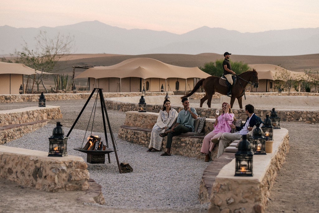 White luxury tent suite in desert with wooden deck, panoramic windows overlooking Moroccan sand dunes and Atlas Mountains at sunset