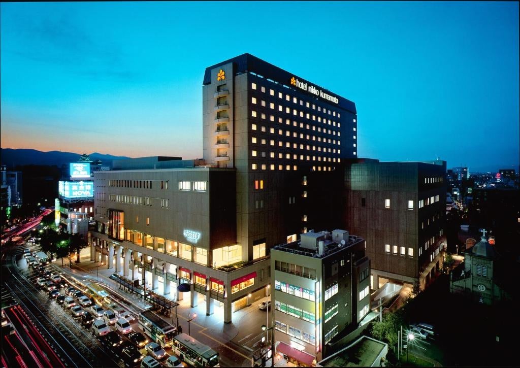 Art deco-style luxury hotel facade in Kumamoto with modern glass windows, elegant entrance canopy, and manicured landscaping at dusk