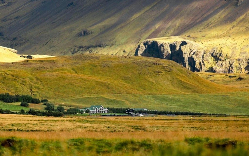 Modern luxury farmhouse hotel with grass-covered roof nestled beneath dramatic Icelandic mountains at golden hour sunset