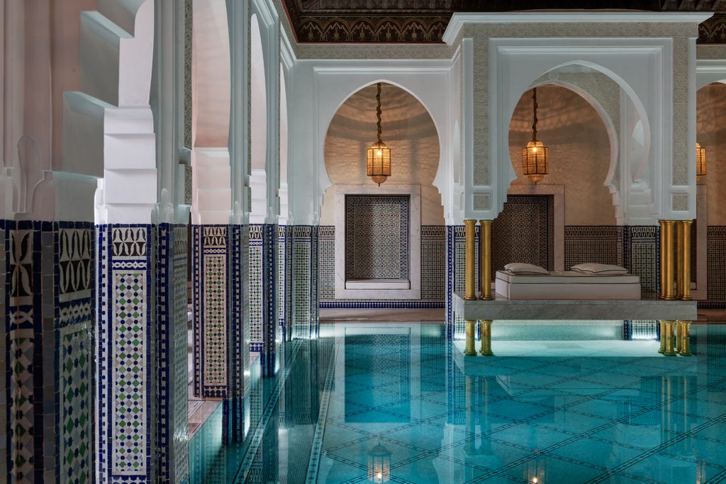 Ornate Moroccan archways frame a tranquil courtyard garden with palm trees and geometric tile fountains at luxury hotel La Mamounia