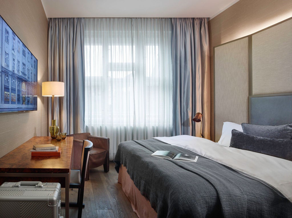 Elegant queen bedroom with plush white bedding, rich dark wood furniture, modern chandelier, and city view at luxury hotel in Prague