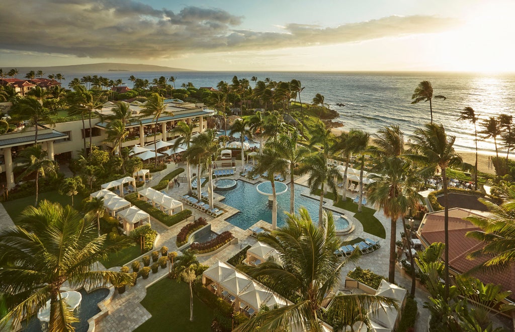 Infinity-edge pool overlooking pristine Wailea Beach, with palm trees and luxury cabanas, against a backdrop of Maui's coastline