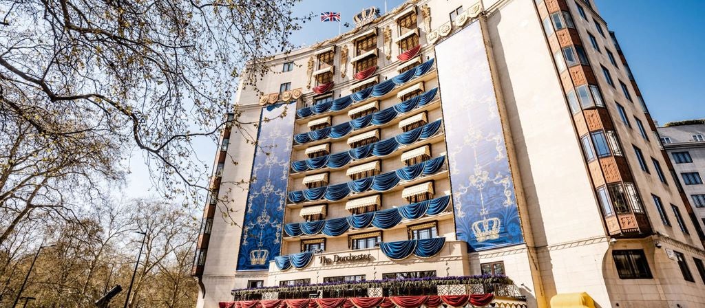 Elegant stone facade of The Dorchester luxury hotel in London with ornate columns, curved balconies and manicured trees lining entrance