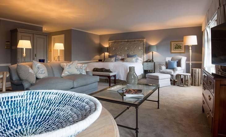 Luxurious hotel suite at Chewton Glen with elegant decor, plush bedding, modern furnishings, and expansive windows overlooking lush countryside landscape.