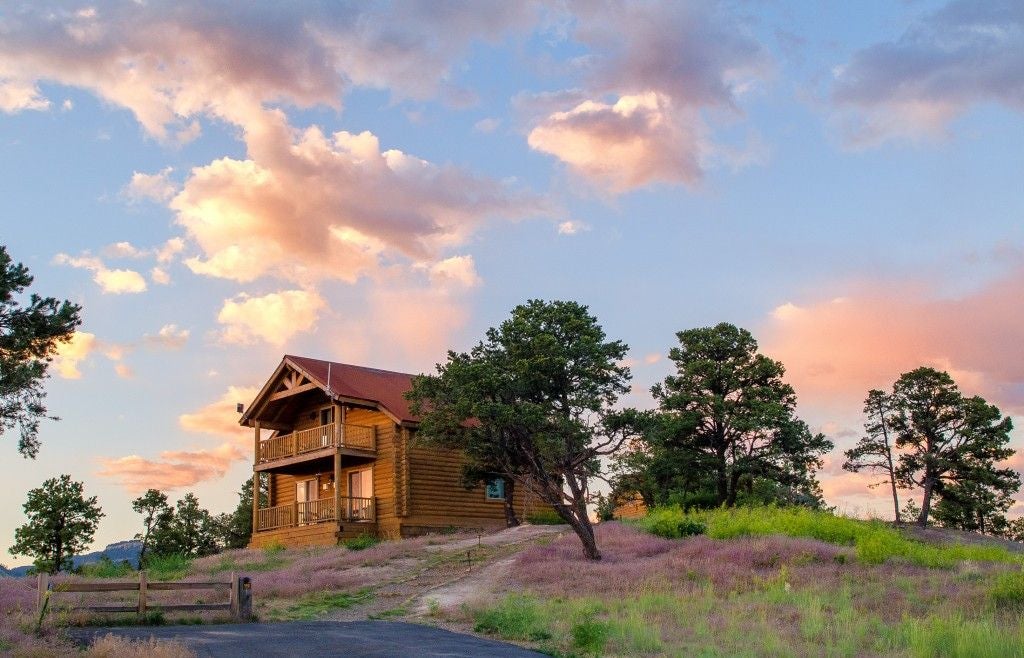 Rustic wooden cabin interior with two comfortable bedrooms, southwestern decor, warm earth tones, large windows overlooking scenic mountain landscape at Zion Mountain Ranch