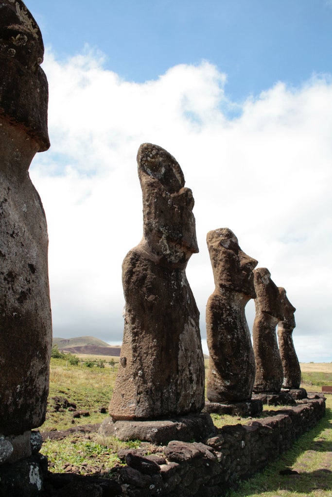 Stone-faced Moai statues at sunrise on Easter Island, overlooking the Pacific Ocean with pink-orange clouds illuminating rugged cliffs