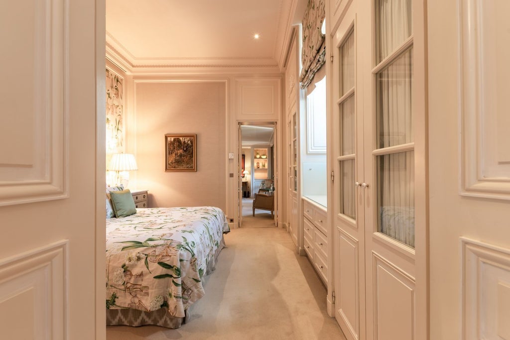 Elegant French junior suite featuring ornate furnishings, crystal chandelier, plush king bed with canopy, and period antiques in soft beige tones