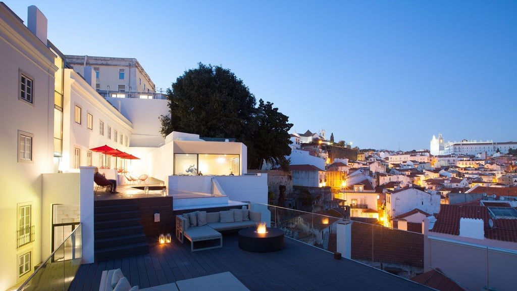 Elegant boutique hotel terrace overlooking Lisbon's historic Alfama district with traditional tiled rooftops and warm sunset lighting