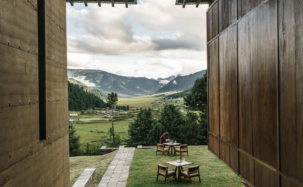 Modern luxury lodge with floor-to-ceiling windows offering panoramic valley views, nestled in misty Bhutanese mountains at sunset