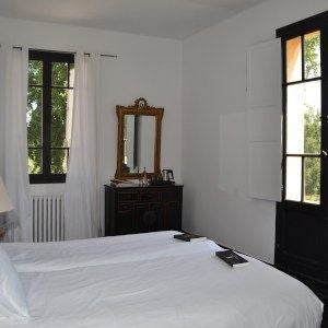 Elegant premium hotel room at Château les Merles, featuring plush white bedding, antique wooden furnishings, and soft natural lighting in French countryside setting