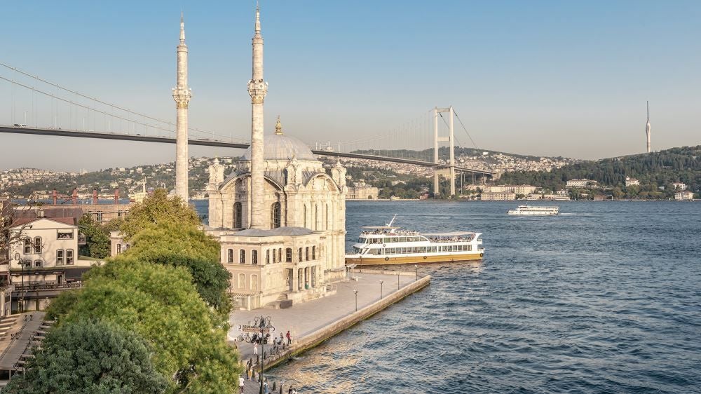 Luxurious contemporary hotel exterior overlooking Bosphorus Strait, featuring sleek glass facade, modern architectural design, and panoramic water views at sunset