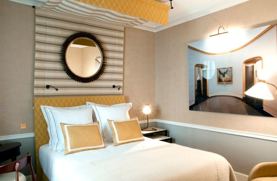 Elegant Paris hotel room with soft gray walls, plush white bedding, decorative headboard, and refined traditional French design elements