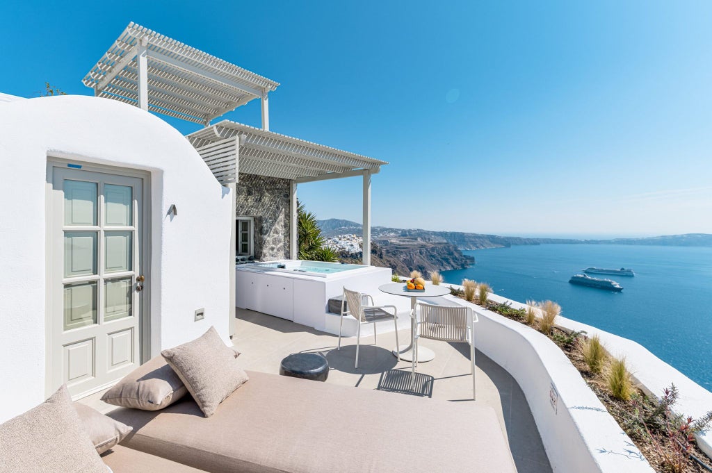 Luxurious white-washed Caldera Suite with arched ceiling, panoramic Aegean Sea views, elegant minimalist decor, and private terrace at Santorini boutique cave hotel