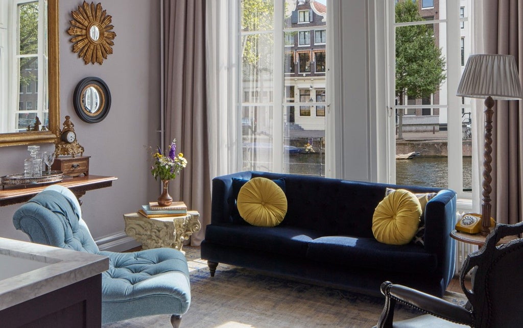 Elegant hotel suite featuring antique decor, herringbone floors, and dramatic floor-to-ceiling windows overlooking Amsterdam's canals