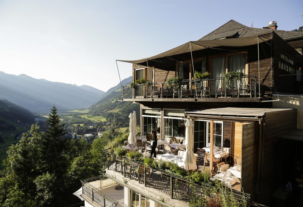 Elegant boutique hotel with modern glass balconies nestled in Austrian Alps, featuring panoramic mountain views and lush gardens