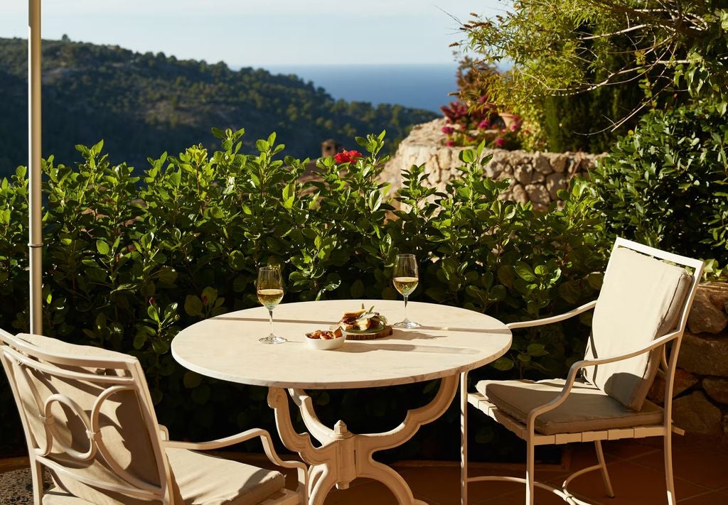 Elegant hotel suite with rustic stone walls, rich hardwood floors, plush king bed, and French doors opening to a private terrace in Mallorca