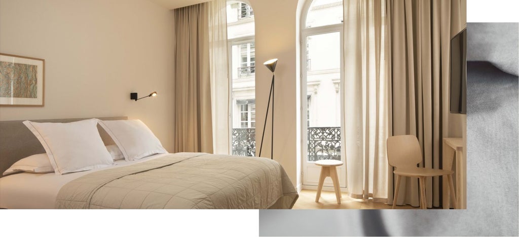 Elegant Paris studio with modern design, plush white bedding, large window, sleek furniture, and soft neutral color palette in boutique hotel room