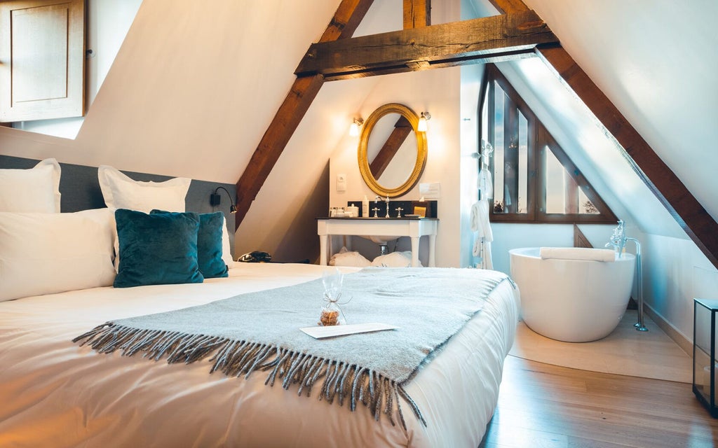 Elegant French countryside hotel room with plush white bedding, soft lighting, and rustic wooden furniture in neutral tones at Manoir de Surville