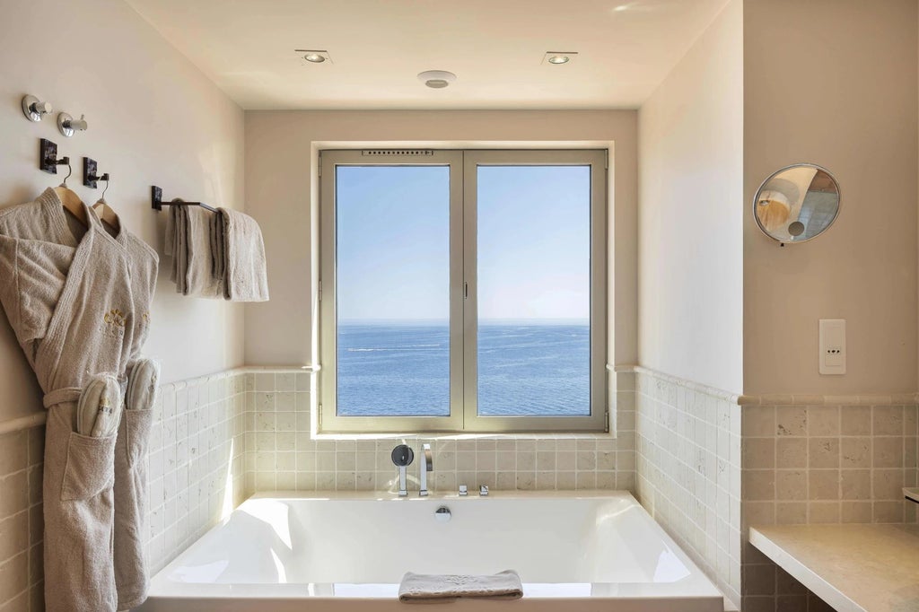 Luxurious rooftop suite overlooking azure Mediterranean waters, featuring elegant white decor, modern furnishings, and panoramic coastal view of French Riviera landscape