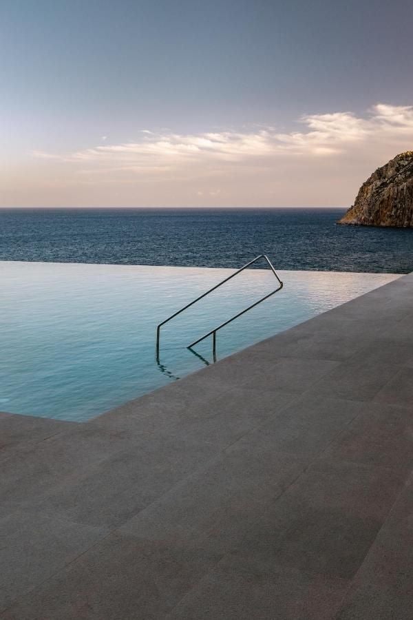 Sleek luxury hotel overlooking Aegean Sea in Greece, featuring infinity pool merging with ocean horizon and modern white architecture