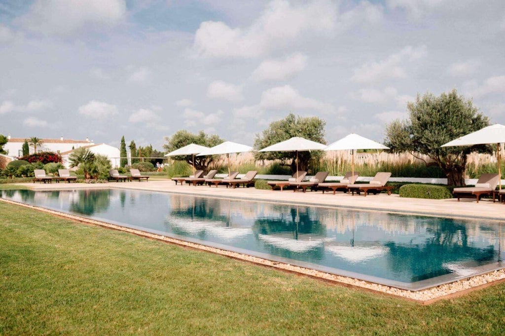 Luxurious white-washed Mediterranean villa nestled in Menorca's rolling countryside, with stone terrace and panoramic views of olive groves and azure coastline