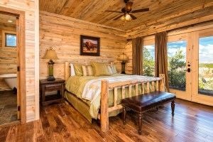 Rustic wooden lodge bedroom at scenset Mountain Ranch with plush bedding, warm earth tones, and panoramic mountain vista through large windows